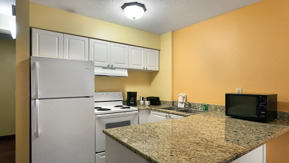A small kitchen area with white appliances, granite countertops, and yellow walls.